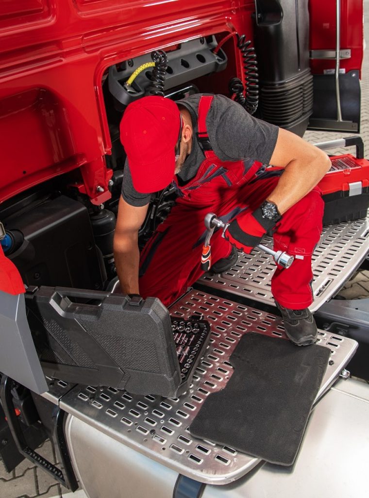 Truck Mechanic Preparing Tools to Start the Repair Caucasian Heavy Duty Vehicle Engineer Sitting on the Back of a Red Semi Truck Taking Necessary Tools Out of the Toolbox to Start Fixing the Issue. Transportation Industry Theme.